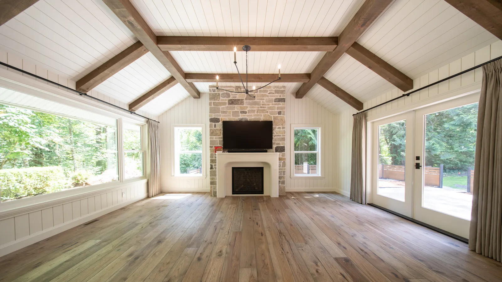 Vaulted great room with exposed beams, stone fireplace, and wide-plank oak flooring