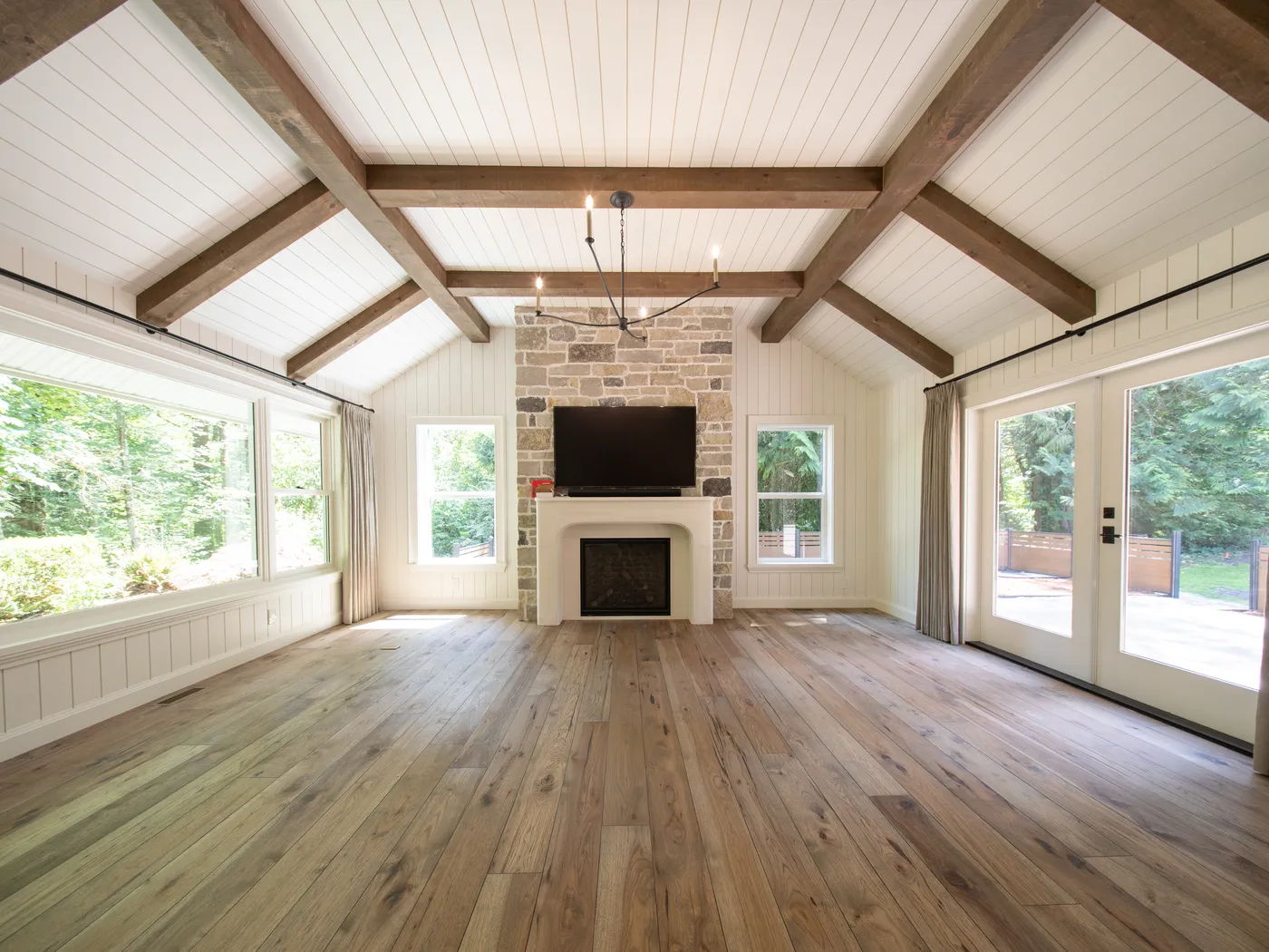 Vaulted great room with exposed beams, stone fireplace, and wide-plank oak flooring