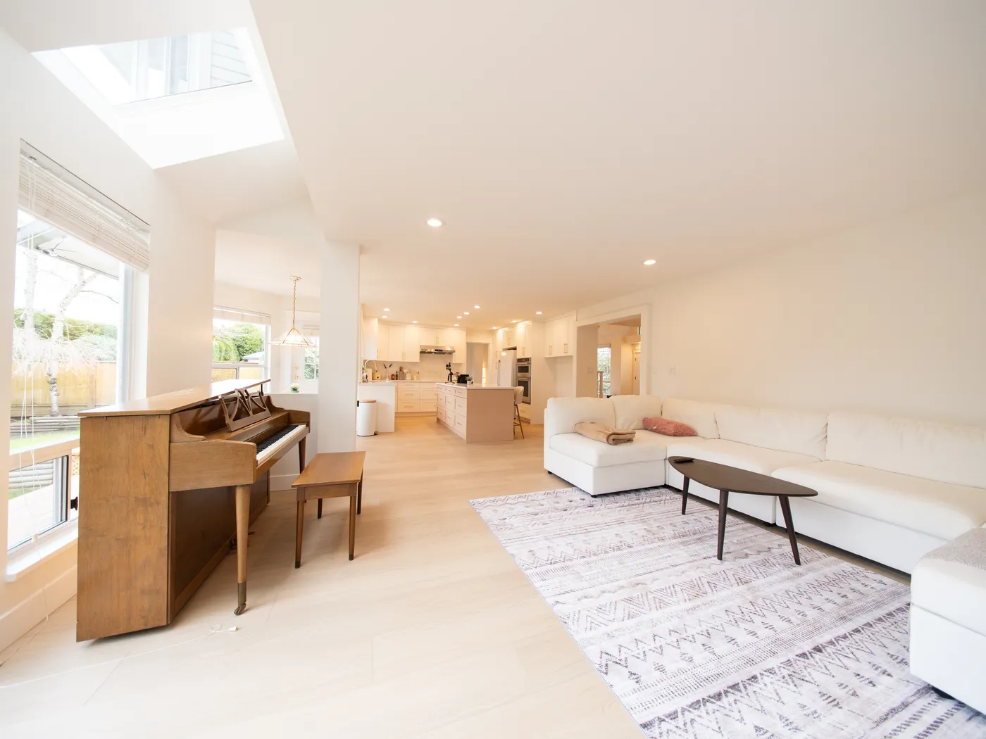 Living room with vaulted ceiling, skylights, and piano